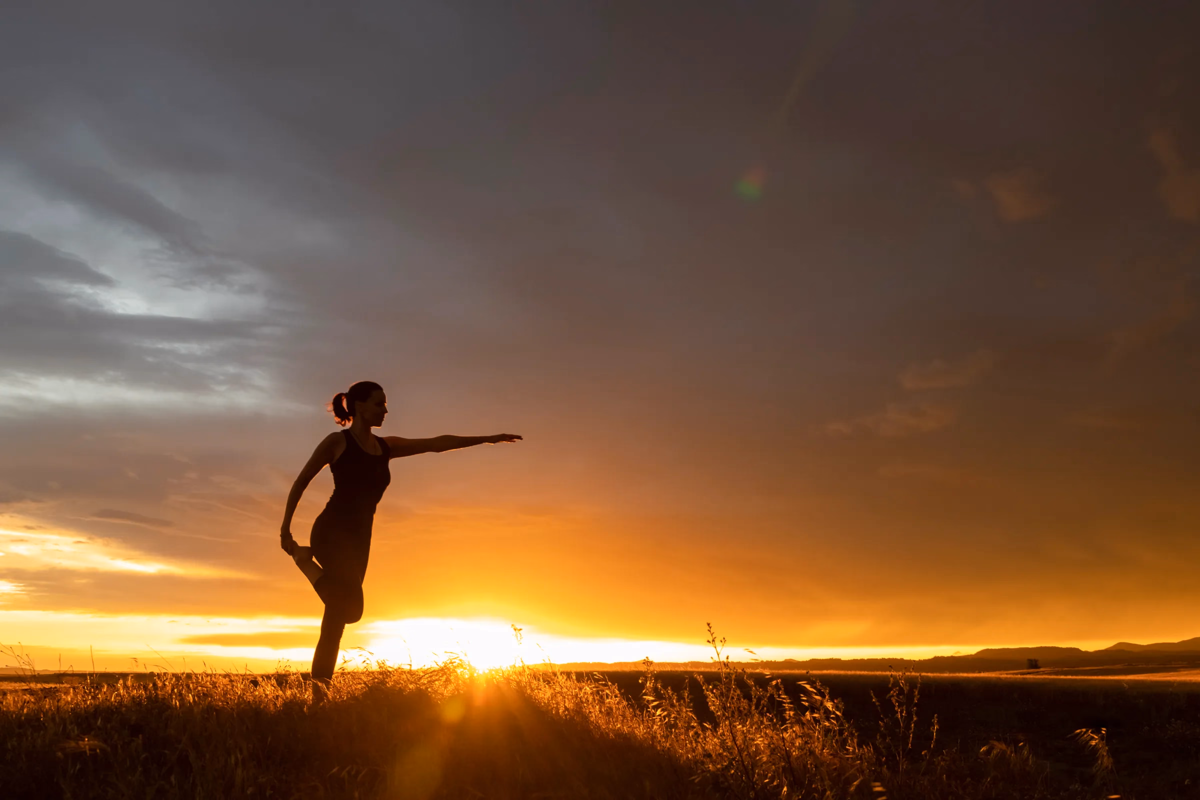 Silueta de una persona en un estiramiento de equilibrio, a contraluz del atardecer.