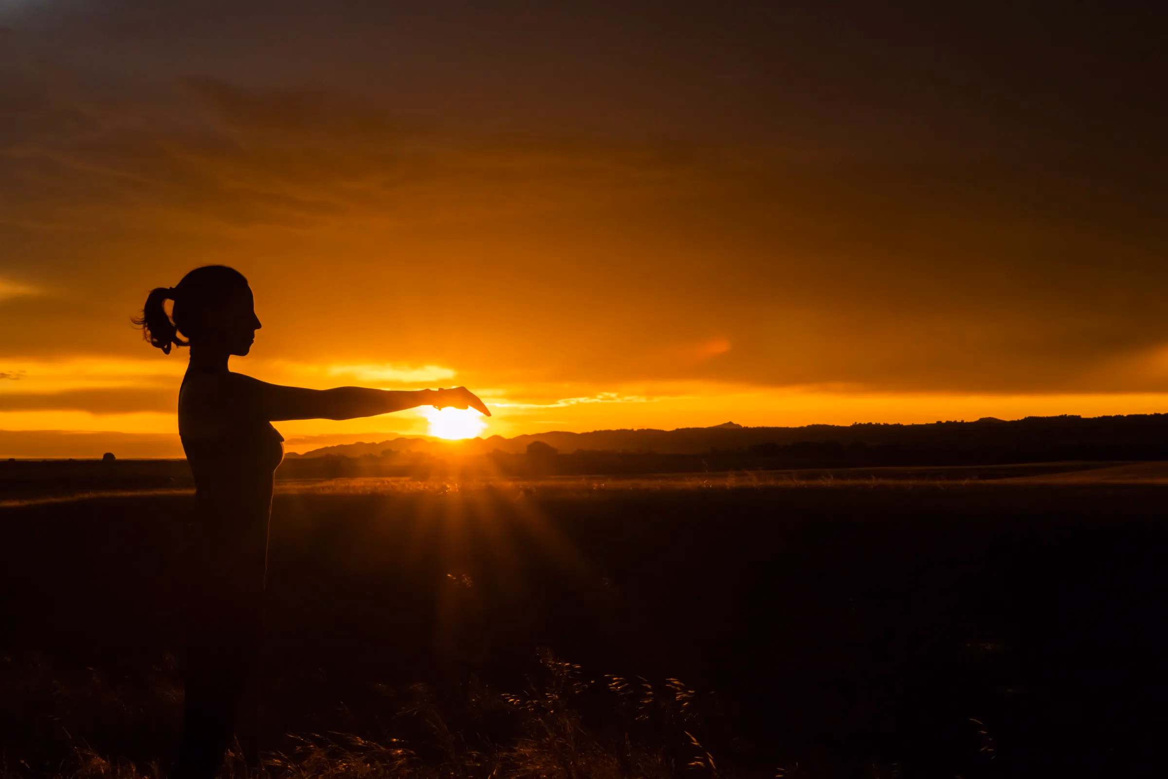 Silueta de una figura estirando el brazo al atardecer, en el campo.
